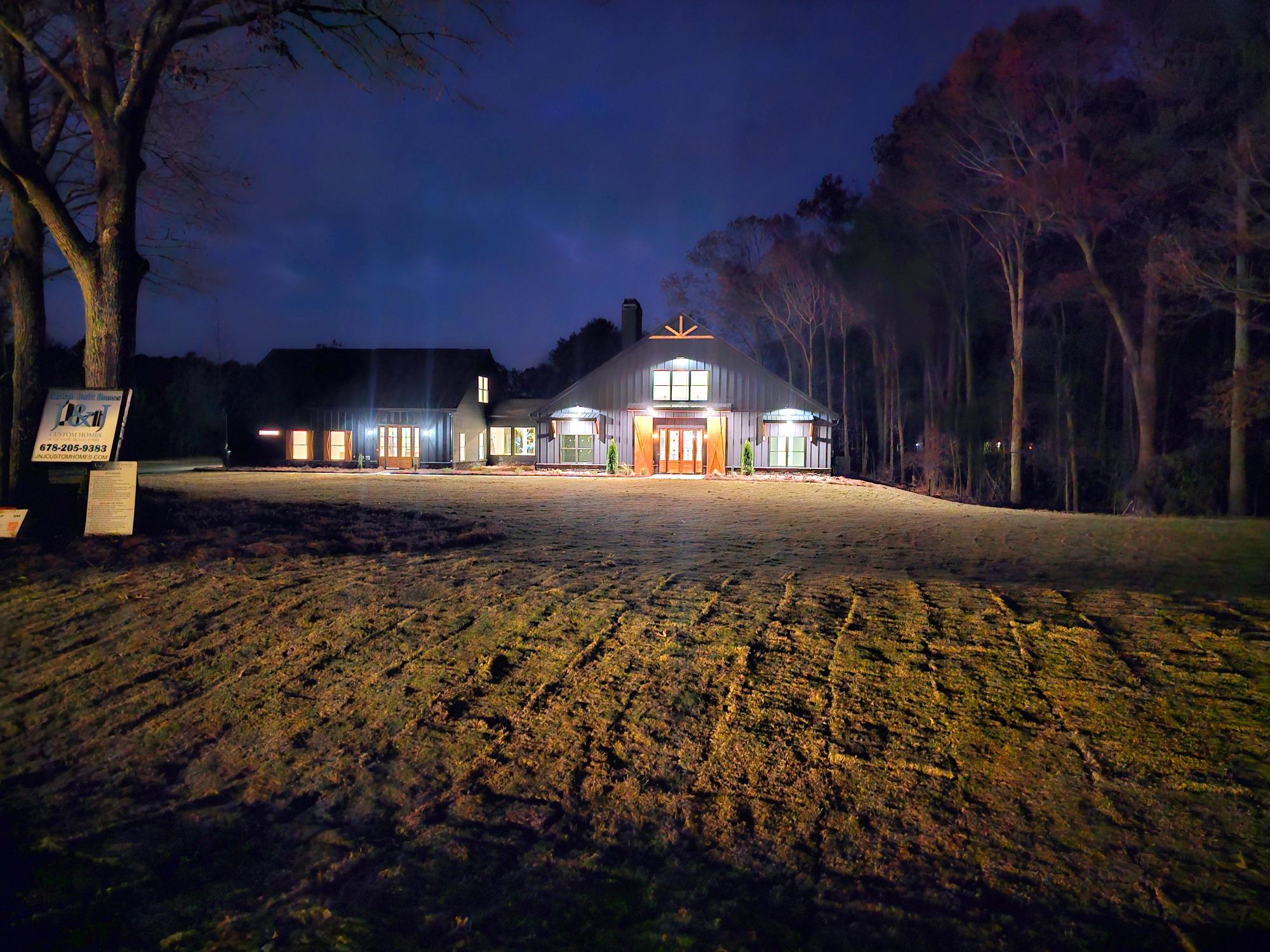 A finished barndominium home with a large yard and trees at night